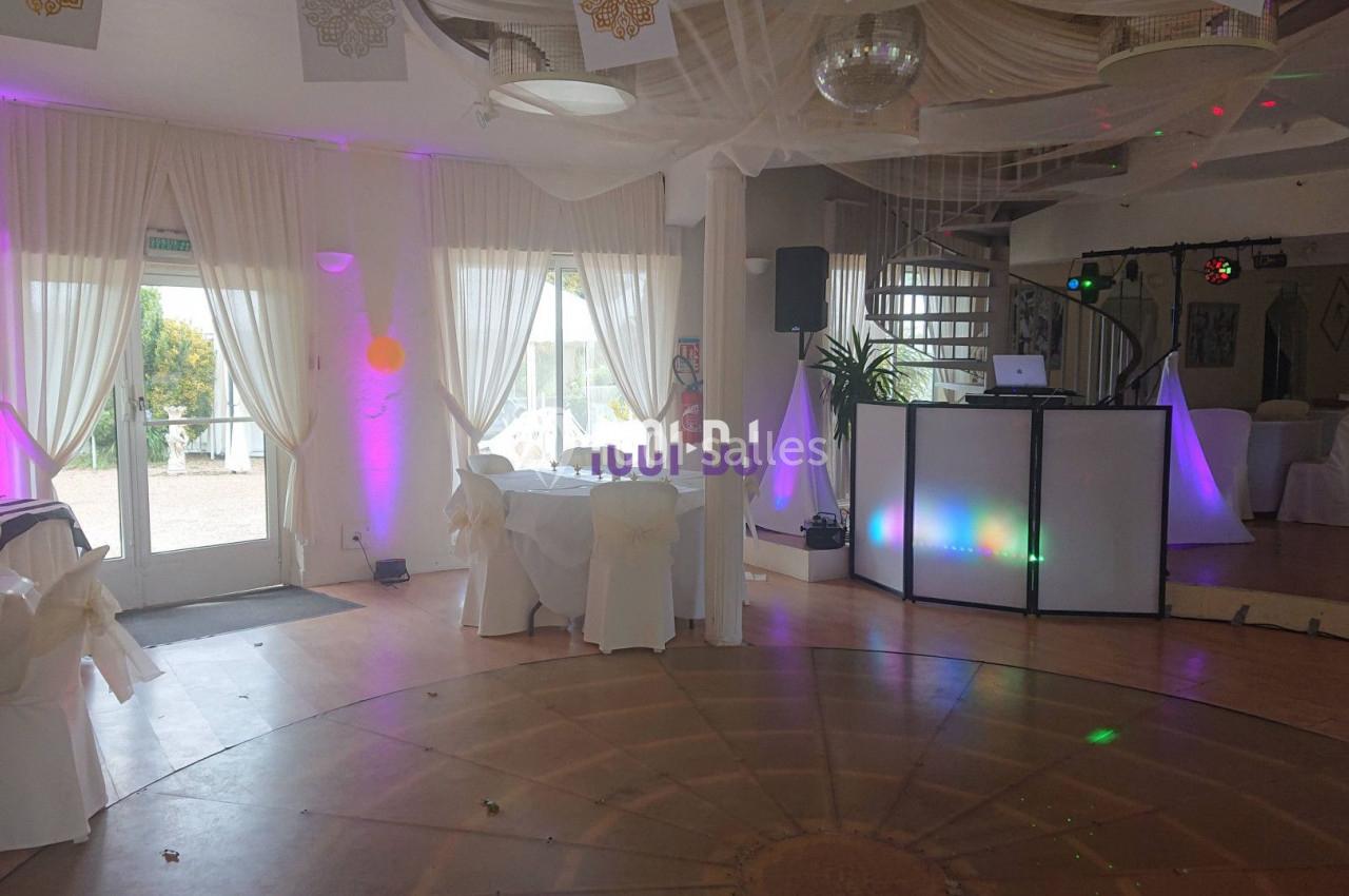 Salle de réception lumineuse avec piste de danse circulaire, tables dressées et éclairages colorés près d'une baie vitrée.