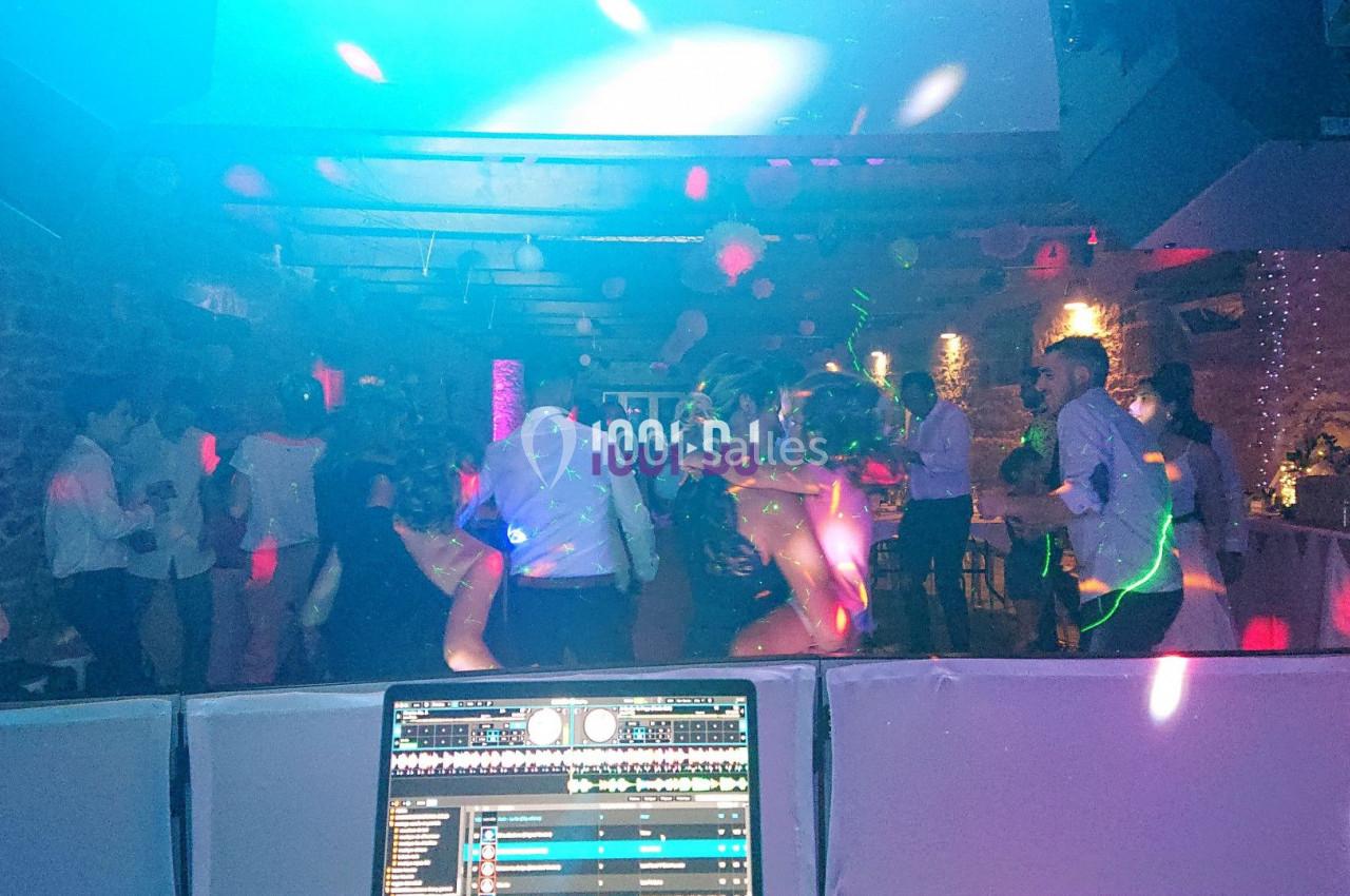 Des personnes dansent dans une salle éclairée par des lumières colorées, vue depuis une table de mixage.