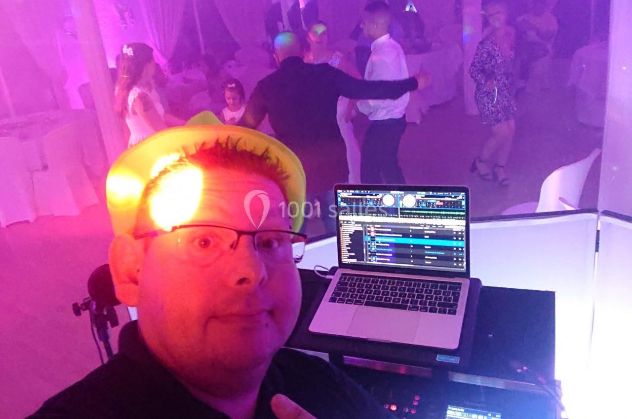 Un DJ anime une soirée dansante avec des invités sur la piste et un ordinateur affichant une playlist musicale.