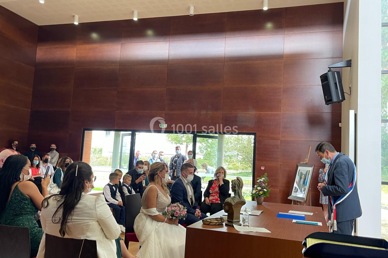 Un couple assis face à un officier municipal lors d'une cérémonie de mariage dans une salle lumineuse.