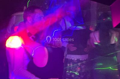 Personnes dansant sous des lumières colorées et des effets de fumée dans une ambiance festive.