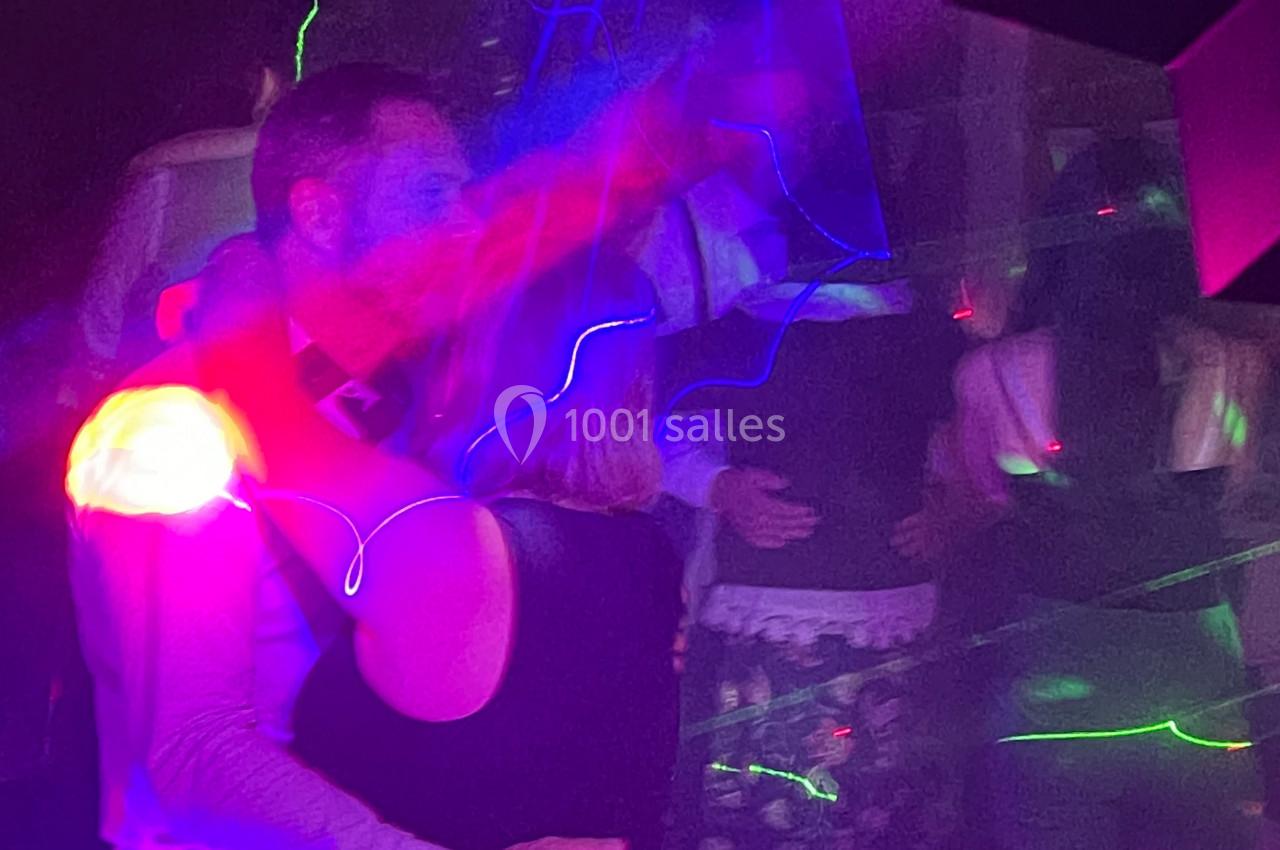 Un couple danse sous des lumières colorées dans une ambiance de fête avec d'autres personnes en arrière-plan.