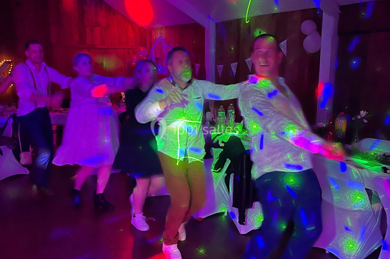 Des personnes dansent en file sous des lumières colorées dans une salle décorée pour une fête.