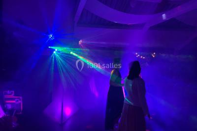 Personnes dansant sous des lumières colorées et des effets de fumée dans une ambiance festive.