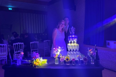 Salle en pierre avec plafond en poutres apparentes, éclairages décoratifs suspendus et équipement audio-visuel installé.