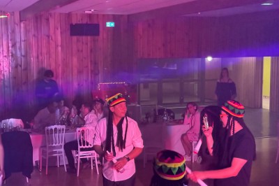 Salle en pierre avec plafond en poutres apparentes, éclairages décoratifs suspendus et équipement audio-visuel installé.