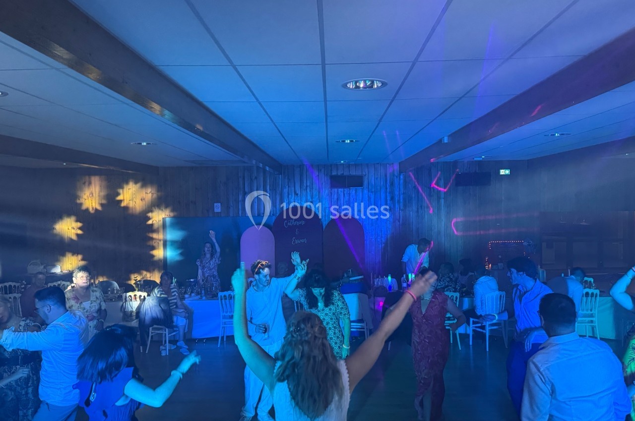 Des personnes dansent sous des lumières colorées dans une salle avec un décor en bois et des tables en arrière-plan.