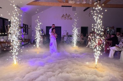 Salle en pierre avec plafond en poutres apparentes, éclairages décoratifs suspendus et équipement audio-visuel installé.