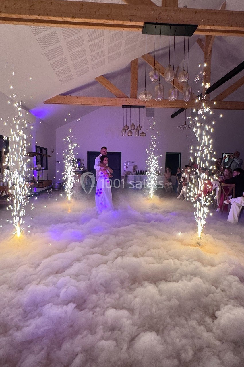 Un couple danse au centre d'une salle éclairée, entouré de fumée au sol et de jets d'étincelles.