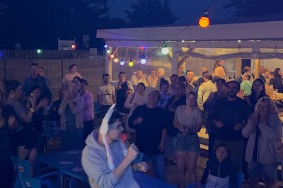 Salle en pierre avec plafond en poutres apparentes, éclairages décoratifs suspendus et équipement audio-visuel installé.