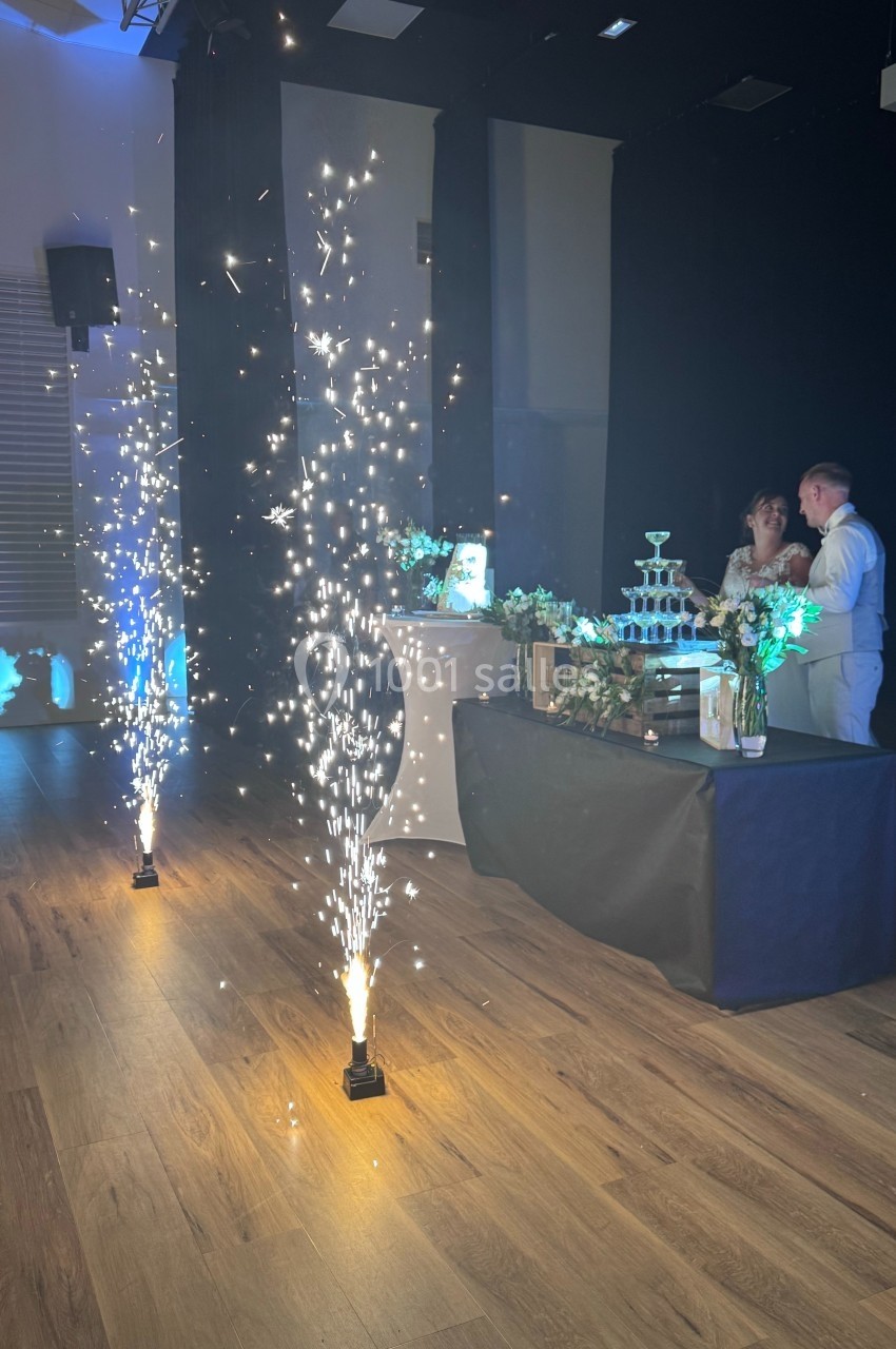 Fontaine de lumière devant une table décorée avec une pyramide de verres, un couple en arrière-plan.