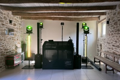 Salle en pierre avec plafond en poutres apparentes, éclairages décoratifs suspendus et équipement audio-visuel installé.