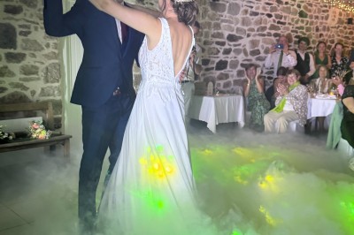 Salle en pierre avec plafond en poutres apparentes, éclairages décoratifs suspendus et équipement audio-visuel installé.