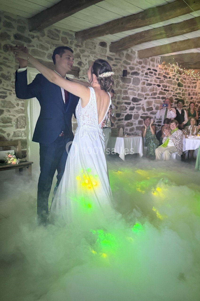 Un couple danse dans une salle en pierre, entouré de fumée et de lumières colorées, sous le regard des invités.