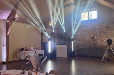 Salle en pierre avec plafond en poutres apparentes, éclairages décoratifs suspendus et équipement audio-visuel installé.