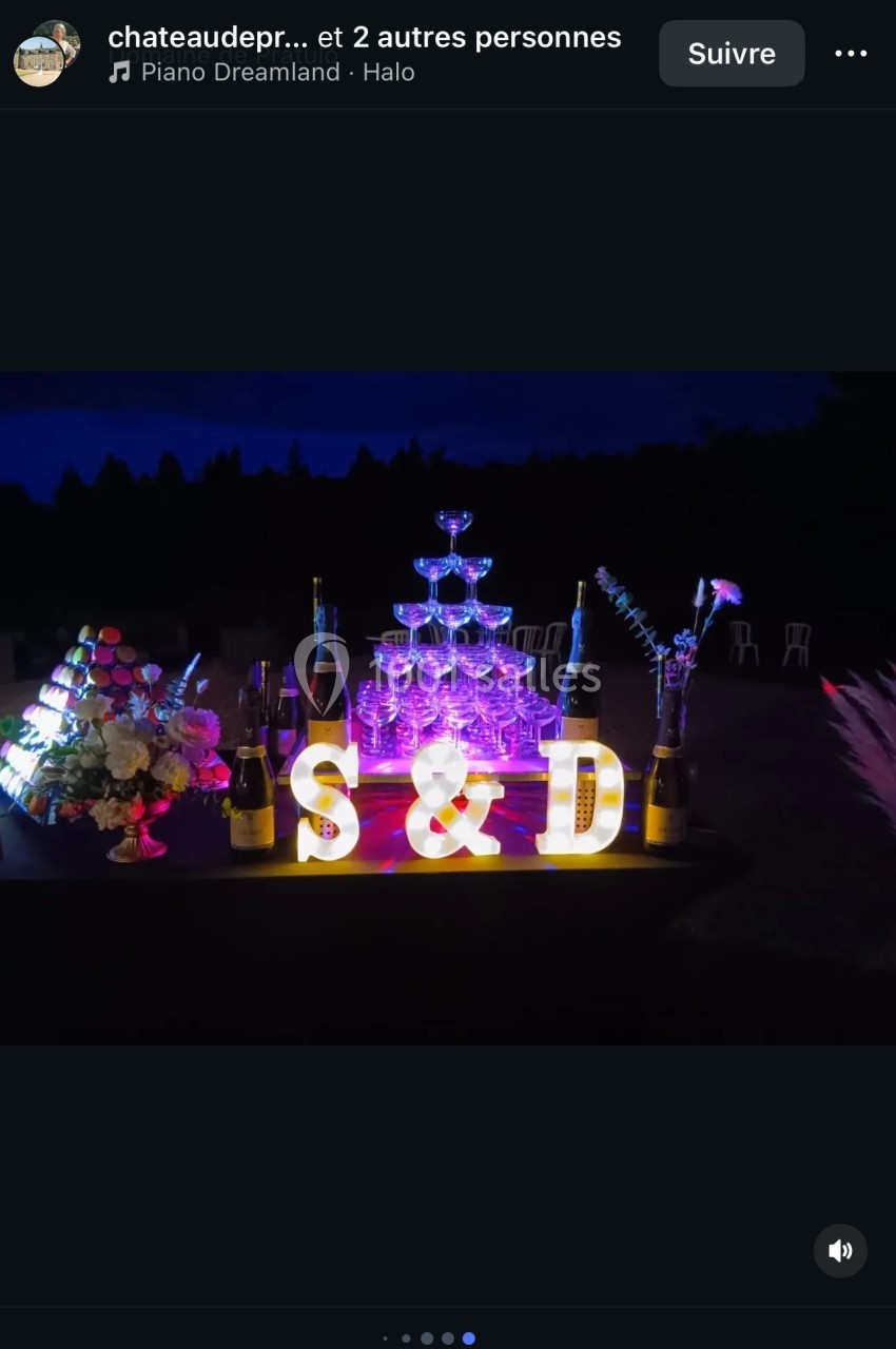 Tour de coupes de champagne illuminée entourée de bouteilles, fleurs et lettres décoratives ’S & D’ dans un décor nocturne.