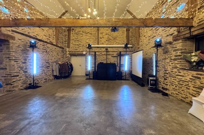 Salle en pierre avec plafond en poutres apparentes, éclairages décoratifs suspendus et équipement audio-visuel installé.