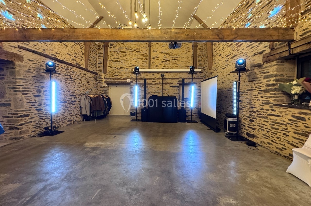 Salle en pierre avec plafond en poutres apparentes, éclairages décoratifs suspendus et équipement audio-visuel installé.