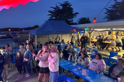 Salle en pierre avec plafond en poutres apparentes, éclairages décoratifs suspendus et équipement audio-visuel installé.