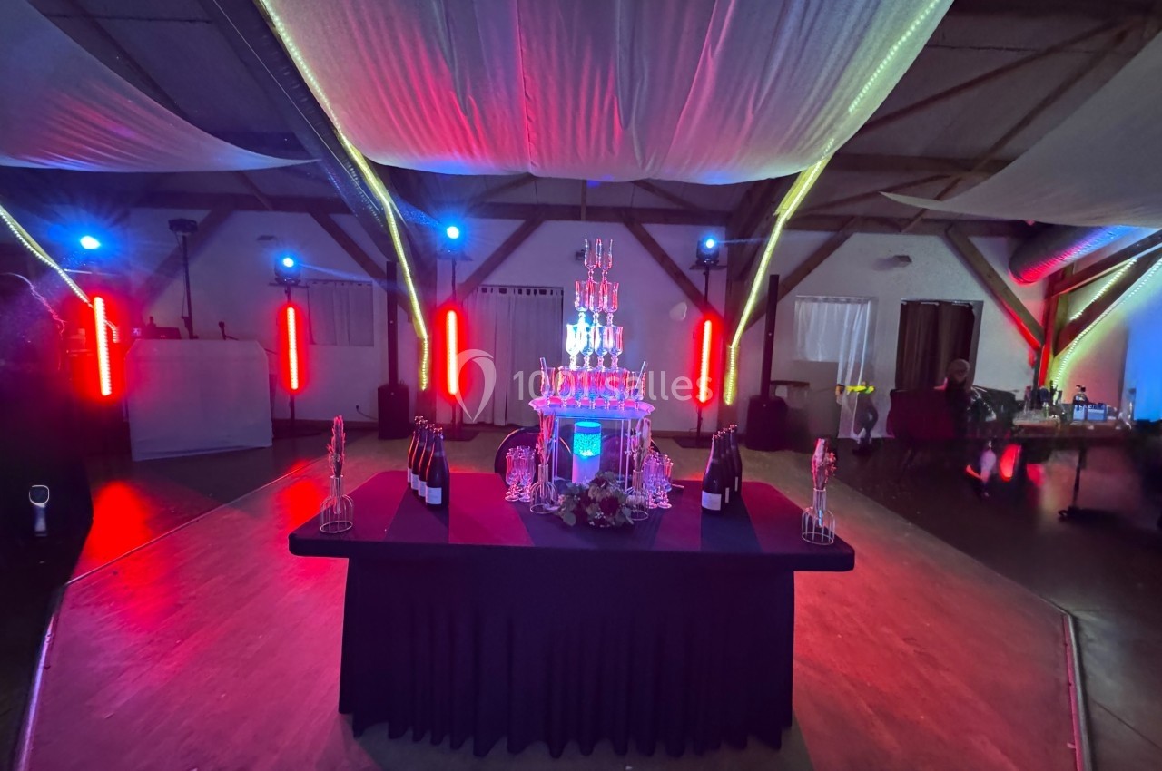 Table décorée avec une pyramide de verres illuminée, entourée de bouteilles et située dans une salle avec éclairage coloré.