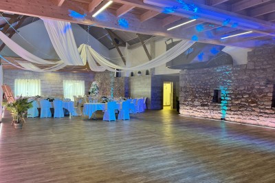 Salle en pierre avec plafond en poutres apparentes, éclairages décoratifs suspendus et équipement audio-visuel installé.