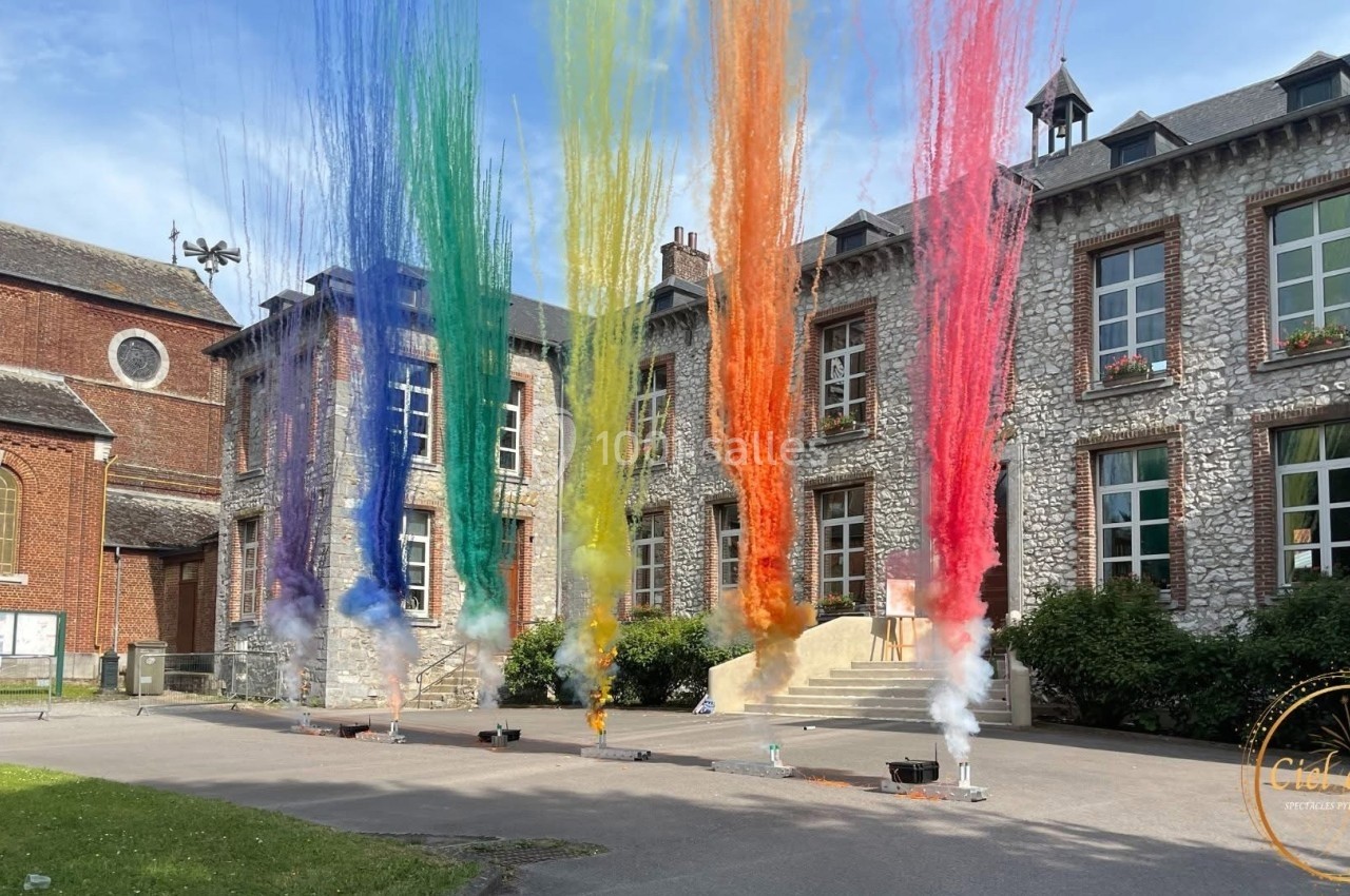 Jets de poudre colorée s'élevant devant un bâtiment en pierre avec des fenêtres et une cour pavée.