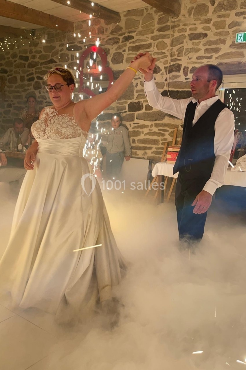 Un couple danse lors d'une fête, entouré de fumée au sol et d'étincelles dans une salle en pierre.