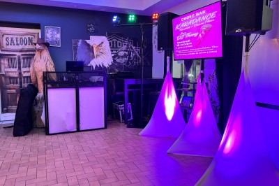 Salle en pierre avec plafond en poutres apparentes, éclairages décoratifs suspendus et équipement audio-visuel installé.