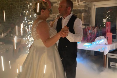 Salle en pierre avec plafond en poutres apparentes, éclairages décoratifs suspendus et équipement audio-visuel installé.