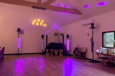 Salle en pierre avec plafond en poutres apparentes, éclairages décoratifs suspendus et équipement audio-visuel installé.