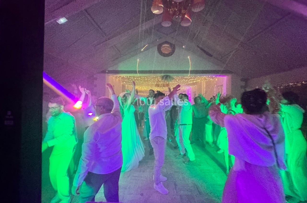 Personnes dansant sous des lumières colorées dans une salle décorée avec des guirlandes lumineuses.