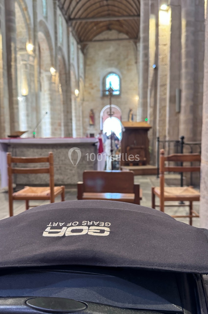 Intérieur d'une église avec des chaises en bois, un autel et une voûte en pierre illuminée par la lumière naturelle.