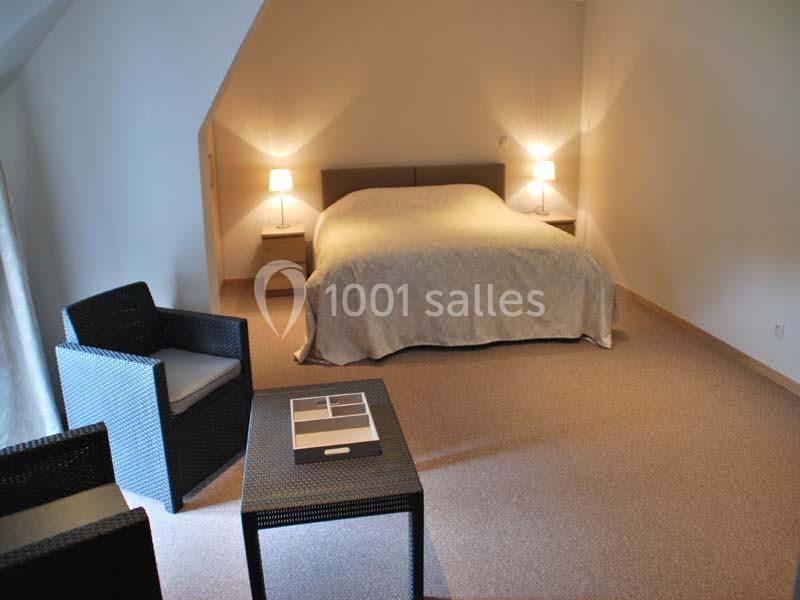 Location salle Ciney (Province de Namur) - Le Domaine d'Achêne #10 Chambre avec lit double, deux lampes de chevet, fauteuils en rotin et table basse sur un sol en moquette beige.