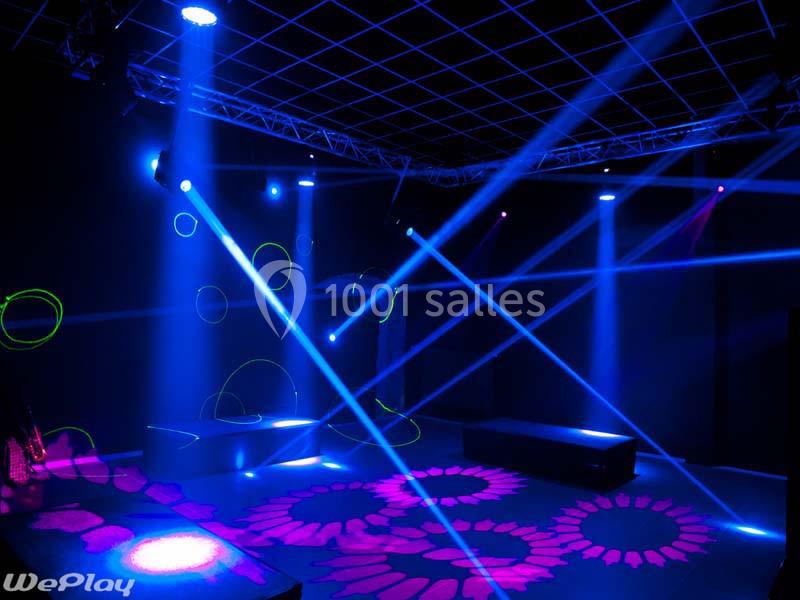 Location salle Ciney (Province de Namur) - Le Domaine d'Achêne #14 Salle sombre illuminée par des projecteurs colorés et des motifs lumineux projetés au sol et sur les murs.