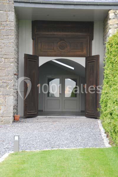 Location salle Ciney (Province de Namur) - Le Domaine d'Achêne #18 Entrée d'un bâtiment avec portes en bois ouvertes, encadrée par des murs en pierre et un chemin de gravier.