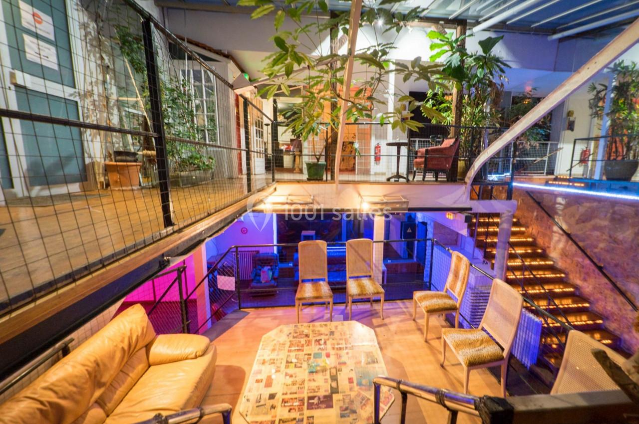 Espace intérieur lumineux avec mezzanine, mobilier varié, plantes et escalier éclairé.