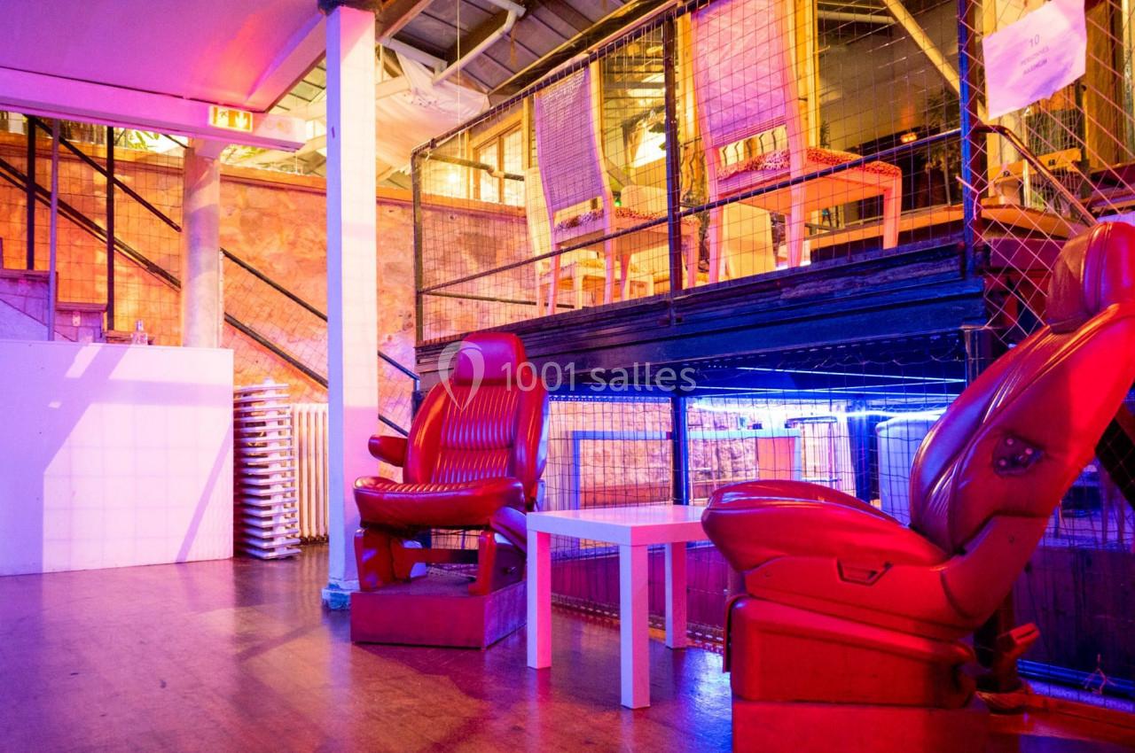 Deux fauteuils rouges devant une table blanche dans un espace industriel avec éclairage coloré.