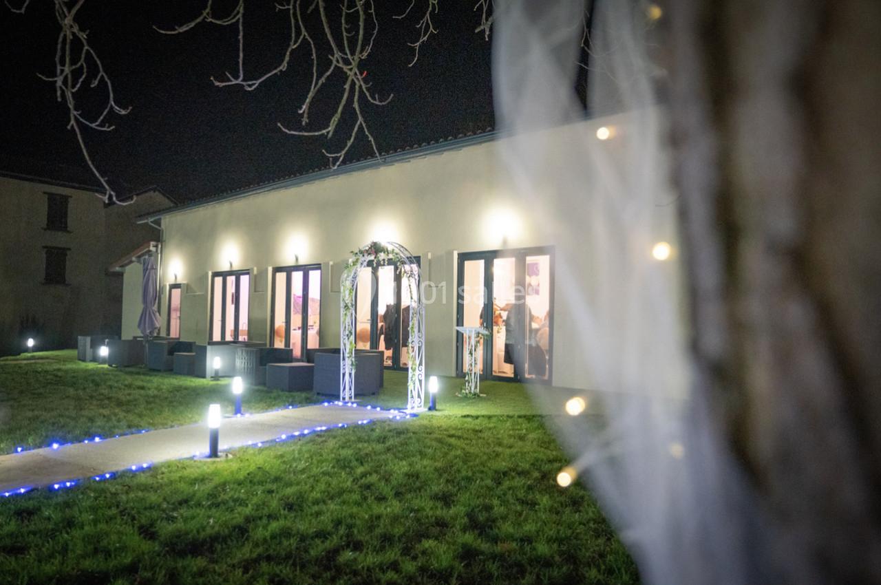 Façade d'un bâtiment éclairé la nuit, avec une arche décorative et un chemin bordé de lumières.