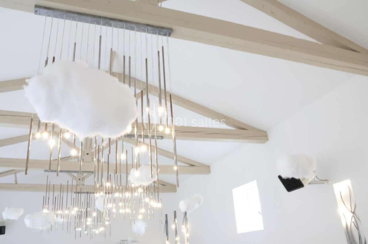 Suspension lumineuse moderne avec des nuages décoratifs blancs accrochée à un plafond en poutres apparentes.