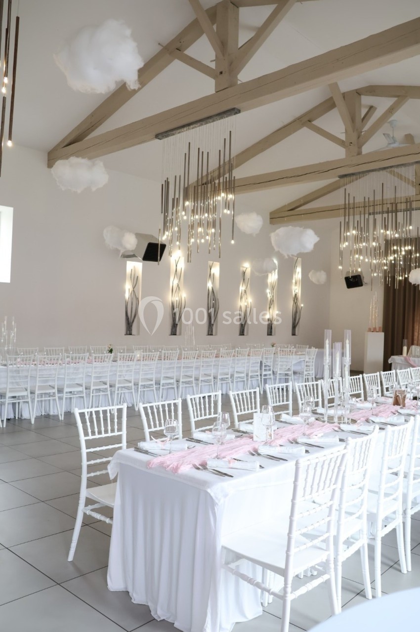 Salle de réception décorée avec des tables blanches alignées, nappes élégantes et éclairage suspendu moderne.