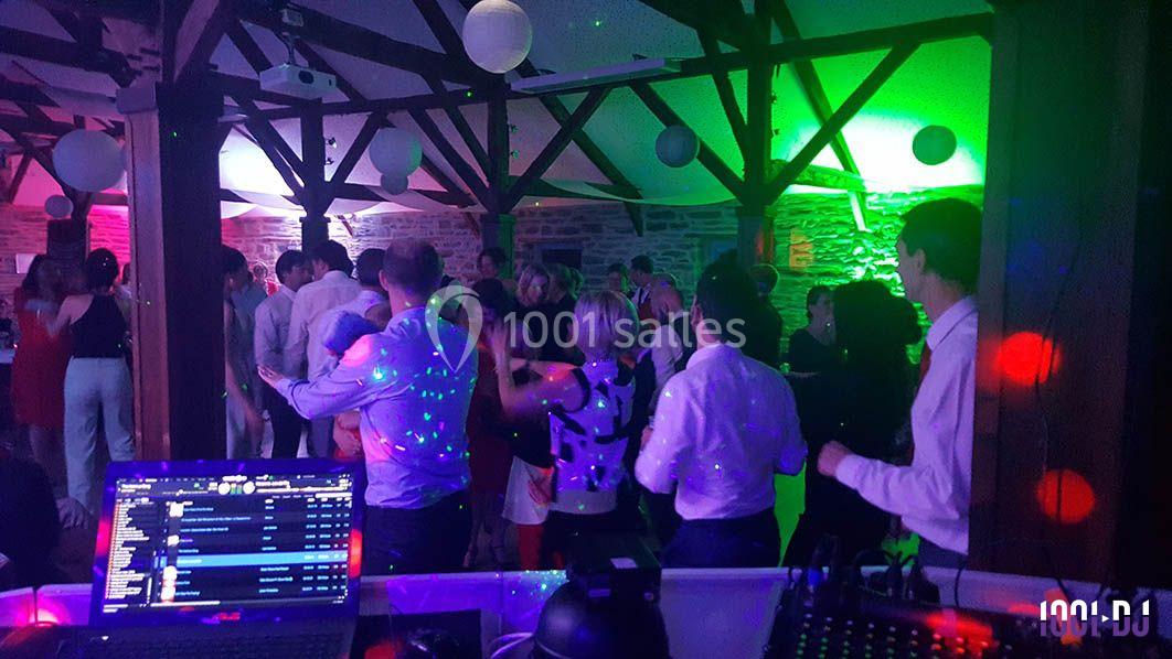 Personnes dansant dans une salle éclairée par des lumières colorées, avec une table de DJ visible au premier plan.