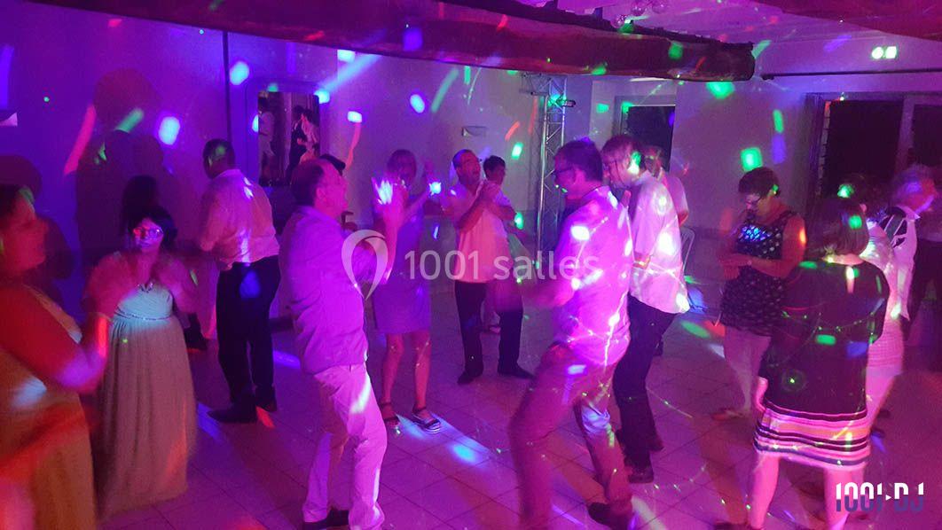 Des personnes dansent dans une salle éclairée par des lumières colorées lors d'une fête ou d'un événement.