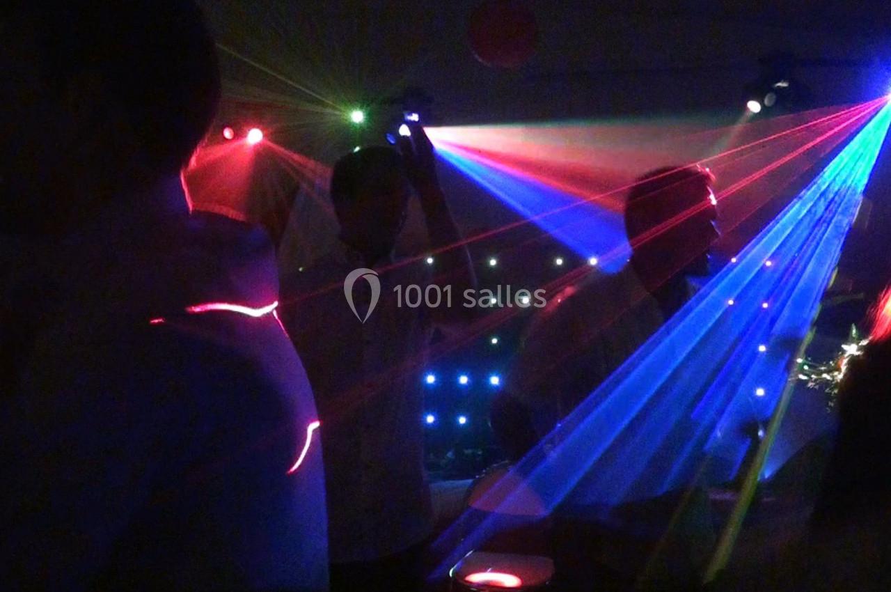 Personnes dansant sous des lumières colorées et des faisceaux laser dans une ambiance de fête nocturne.