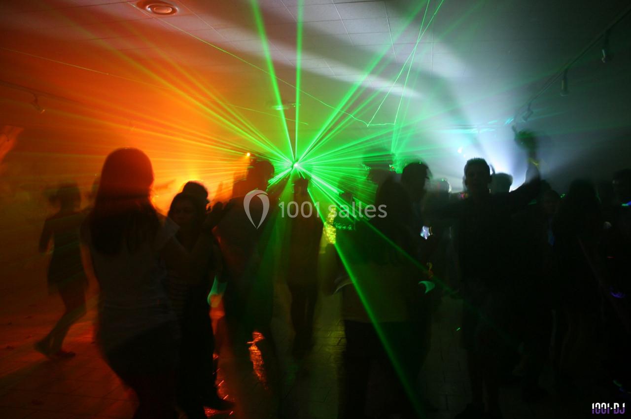 Personnes dansant dans une salle sombre illuminée par des faisceaux lumineux colorés verts et orange.