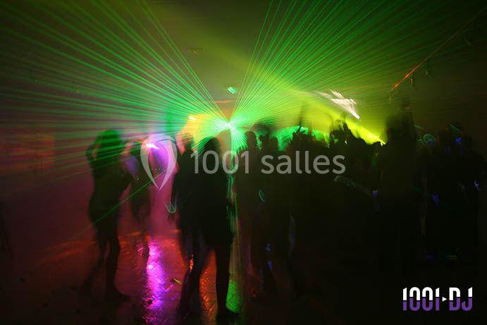 Personnes dansant dans une ambiance sombre avec des jeux de lumières laser verts et jaunes.