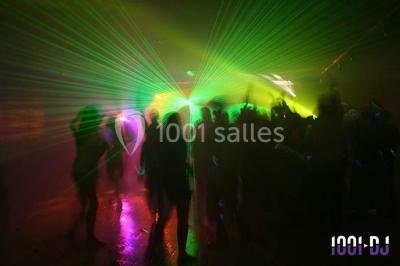 Salle de réception décorée avec des tables rondes, nappes blanches, chaises ornées de nœuds beige et éclairage vert.