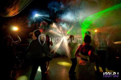Salle de réception décorée avec des tables rondes, nappes blanches, chaises ornées de nœuds beige et éclairage vert.