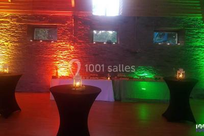 Salle de réception décorée avec des tables rondes, nappes blanches, chaises ornées de nœuds beige et éclairage vert.