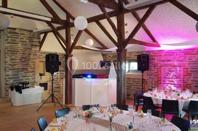 Salle de réception décorée avec des tables rondes, nappes blanches, chaises ornées de nœuds beige et éclairage vert.