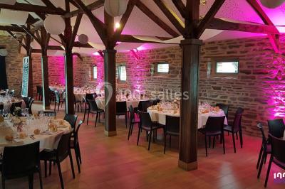 Salle de réception décorée avec des tables rondes, nappes blanches, chaises ornées de nœuds beige et éclairage vert.